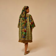 Woman wearing a colorful patterned dress and headscarf on a beige background