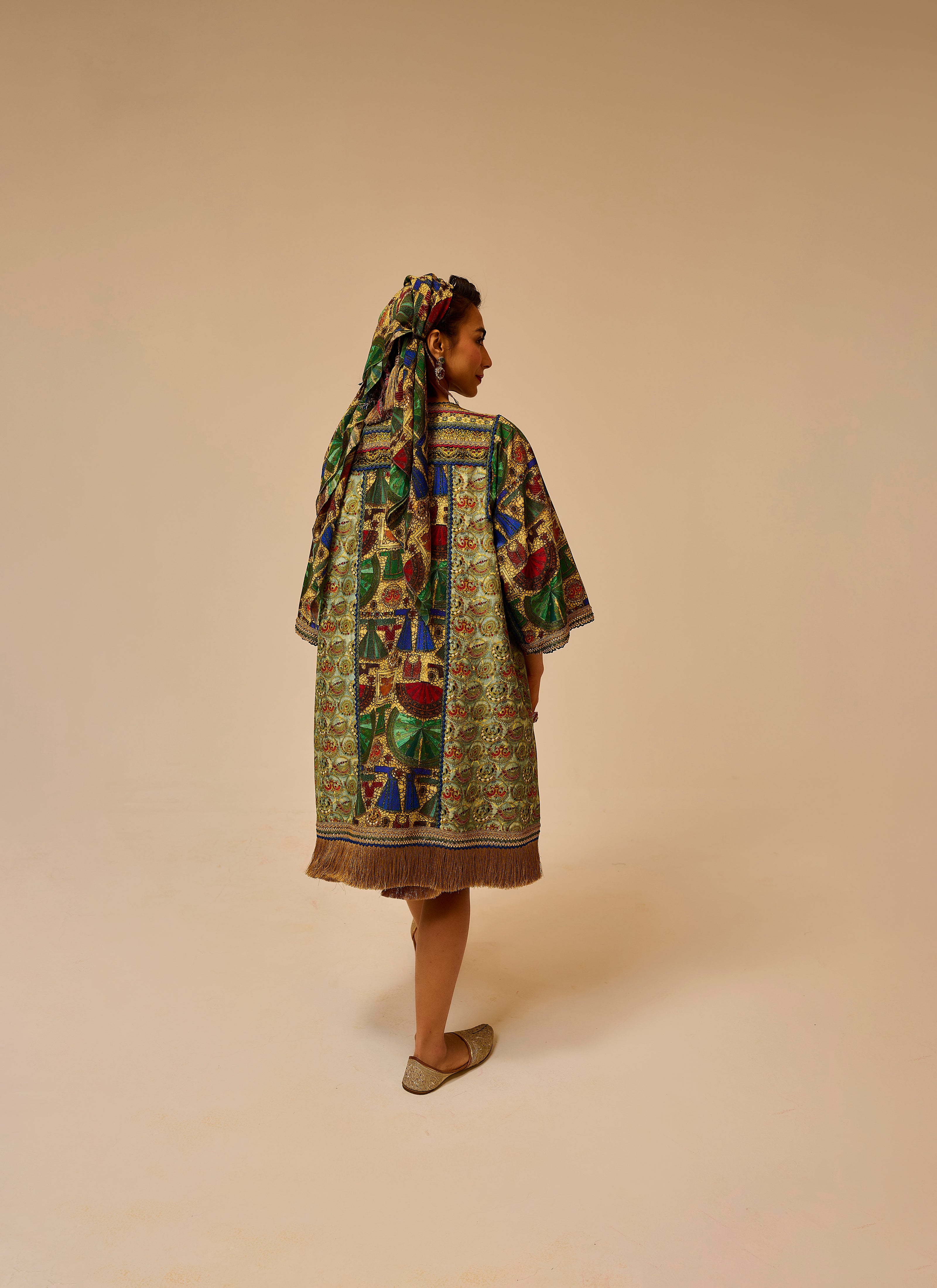 Woman wearing a colorful patterned dress and headscarf on a beige background