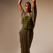 Woman in a traditional outfit with a patterned top and long skirt against a beige background