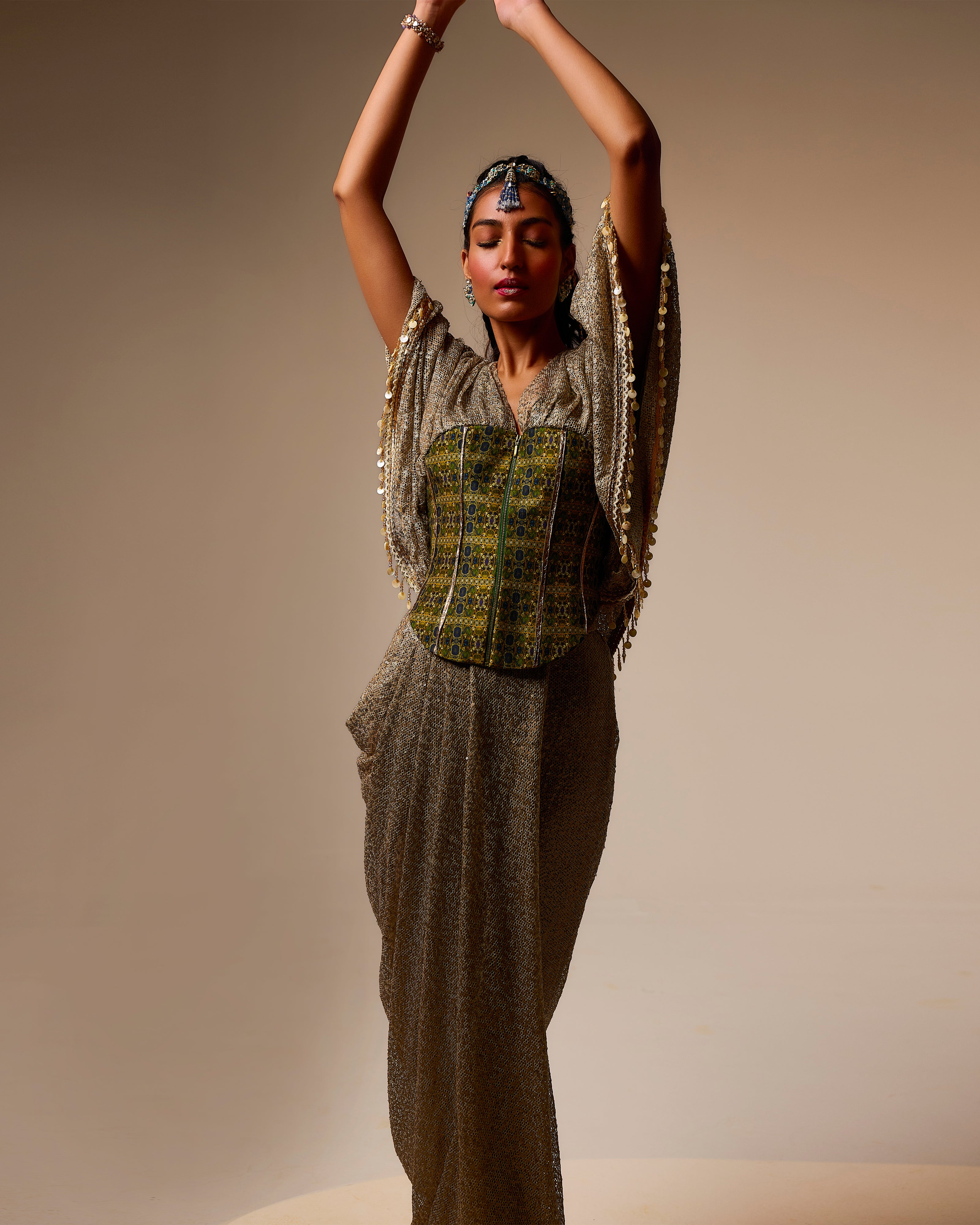 Woman in a traditional outfit with a patterned top and long skirt against a beige background