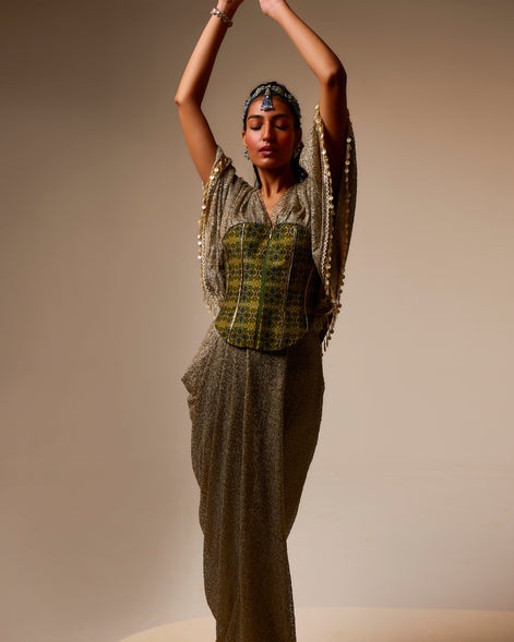 Woman in a traditional outfit with a patterned top and long skirt against a beige background