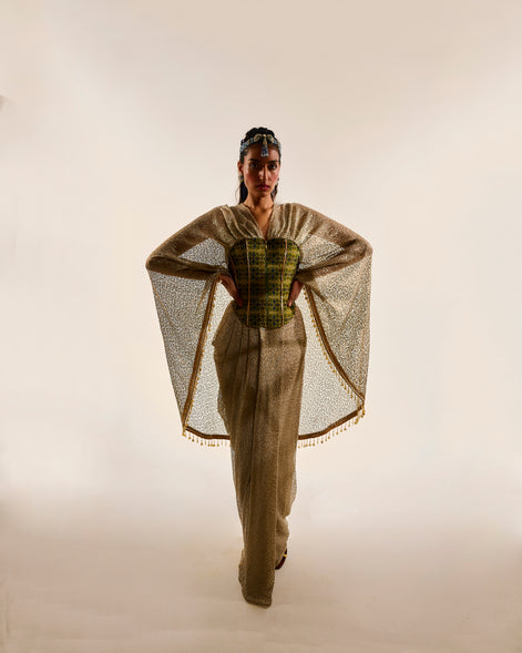 Model wearing a stylish outfit with a cape and patterned top on a plain background