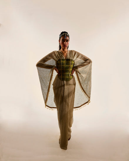Model wearing a stylish outfit with a cape and patterned top on a plain background