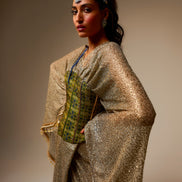 Woman wearing a traditional outfit with a gold and green patterned top against a plain background