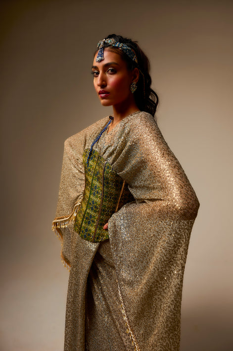 Woman wearing a traditional outfit with a gold and green patterned top against a plain background