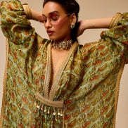 Woman wearing a traditional outfit with intricate patterns and jewelry against a beige background
