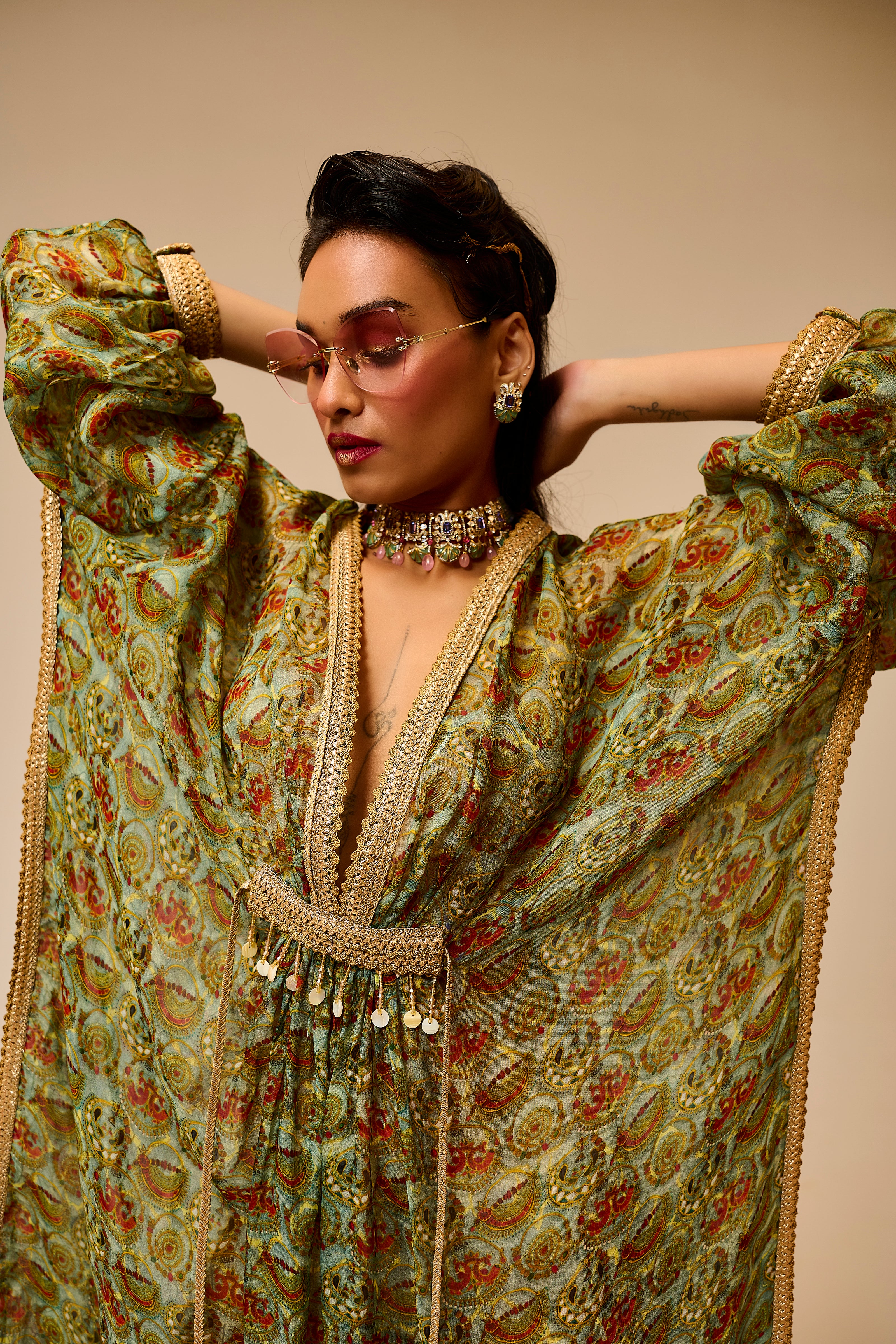 Woman wearing a traditional outfit with intricate patterns and jewelry against a beige background