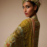 Woman wearing an ornate, patterned outfit with a matching headscarf against a neutral background