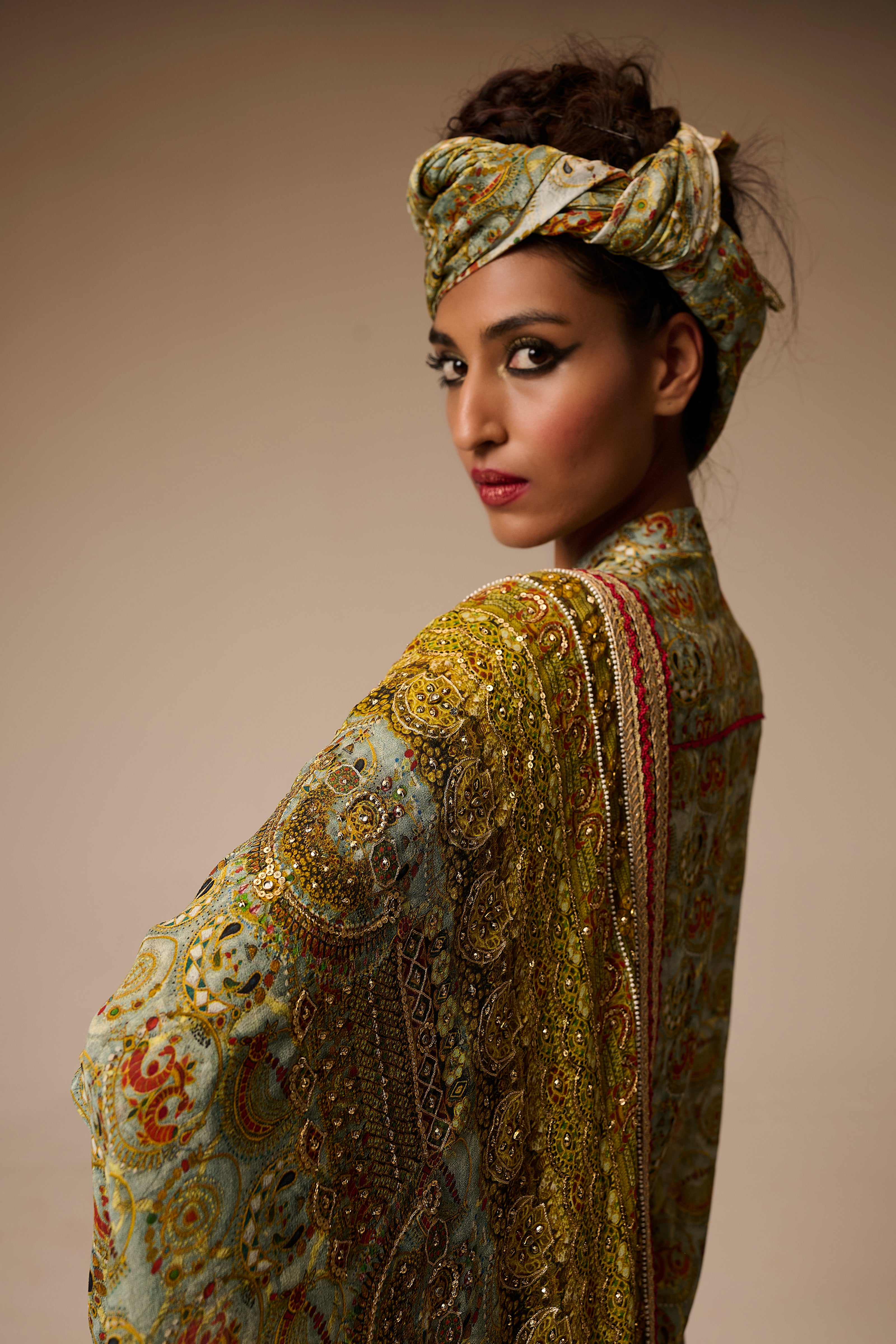 Woman wearing an ornate, patterned outfit with a matching headscarf against a neutral background