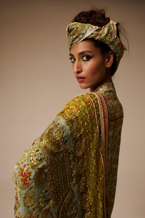 Woman wearing an ornate, patterned outfit with a matching headscarf against a neutral background