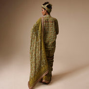 Woman wearing a traditional green saree with a patterned blouse against a beige background