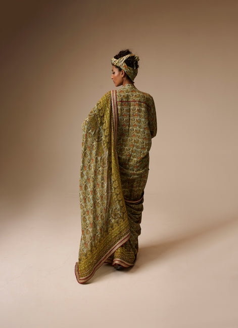 Woman wearing a traditional green saree with a patterned blouse against a beige background