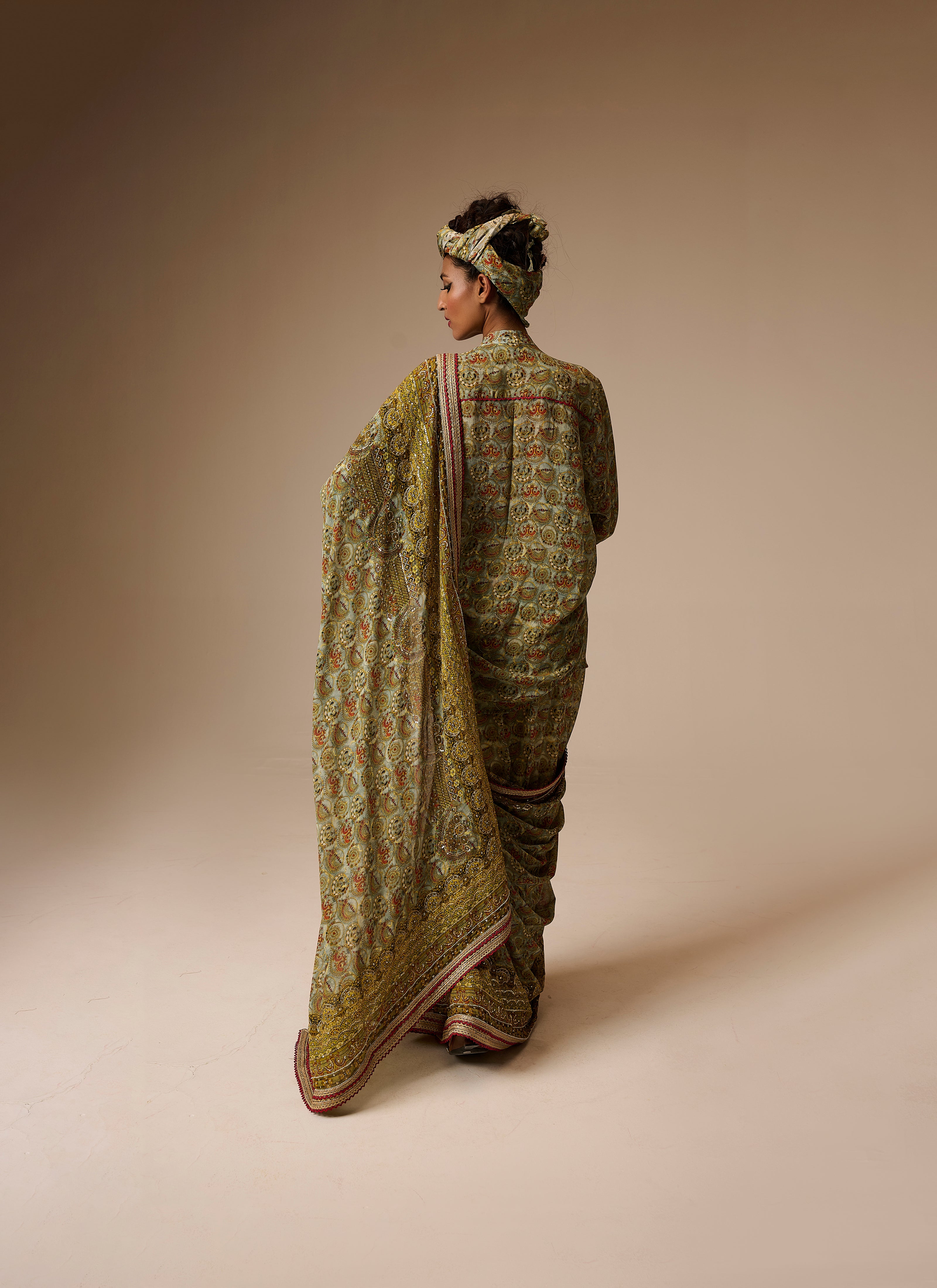 Woman wearing a traditional green saree with a patterned blouse against a beige background
