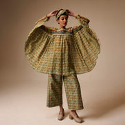 Person wearing a floral dress and pants with a headscarf on a beige background