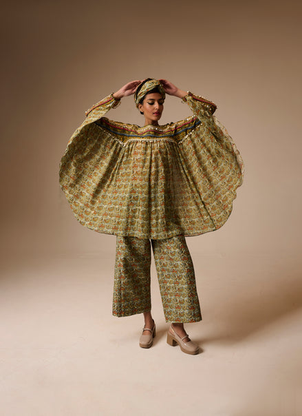 Person wearing a floral dress and pants with a headscarf on a beige background