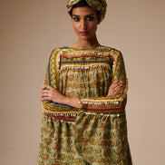 Woman wearing a patterned outfit with a turban against a beige background