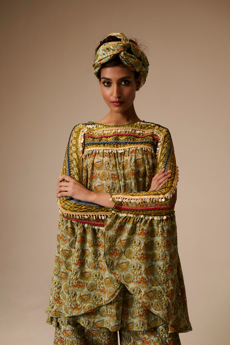 Woman wearing a patterned outfit with a turban against a beige background