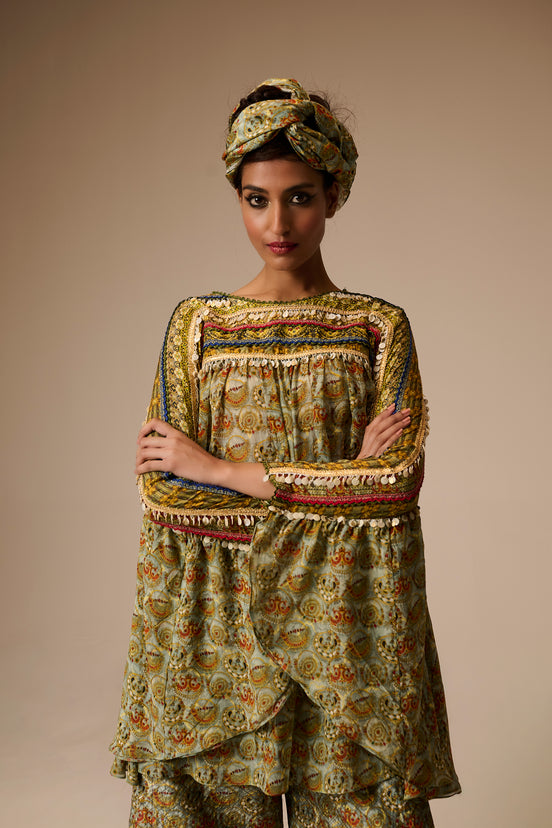 Woman wearing a patterned outfit with a turban against a beige background