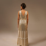 Woman wearing a long, elegant dress with intricate detailing on a plain background