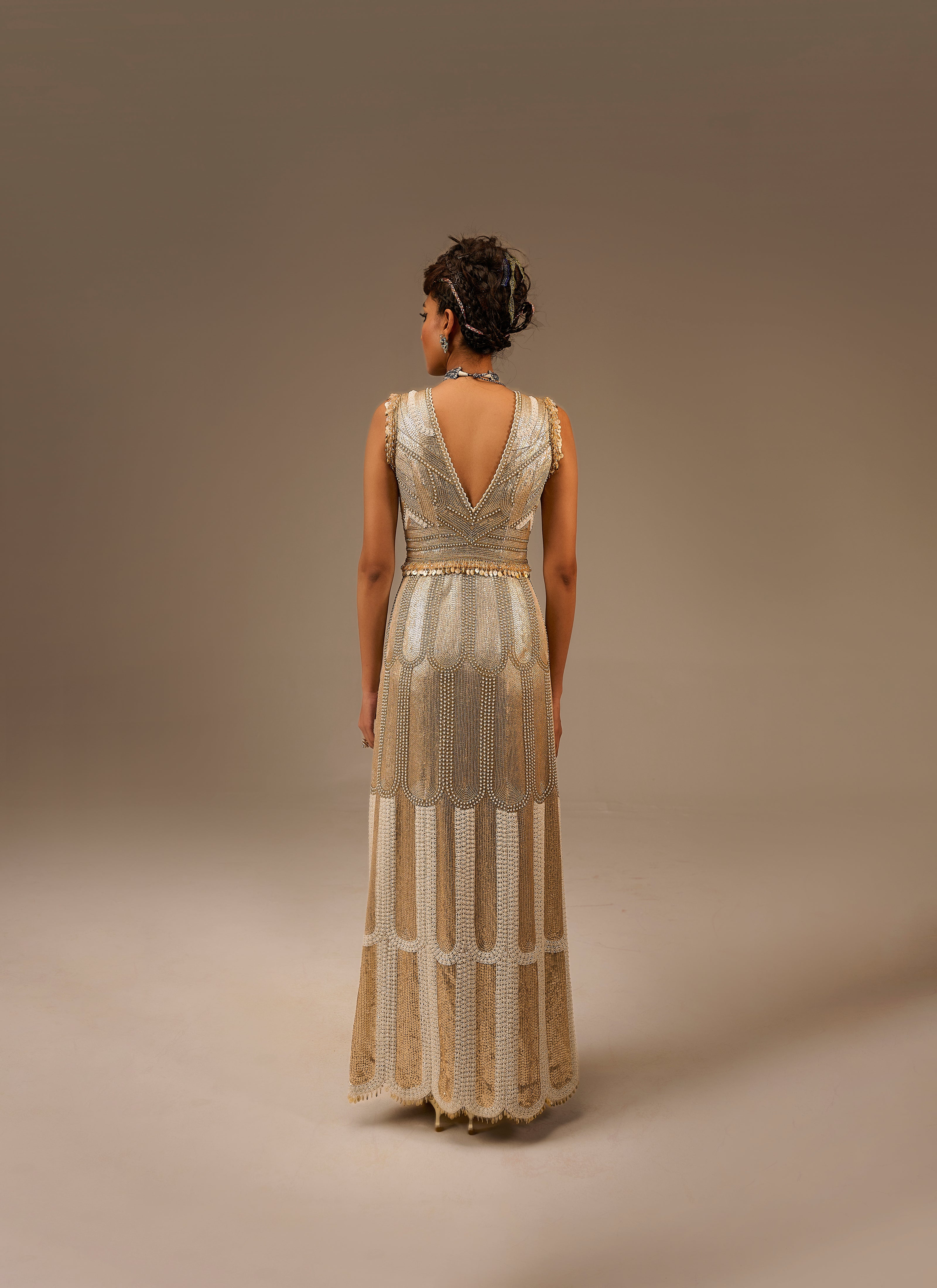 Woman wearing a long, elegant dress with intricate detailing on a plain background