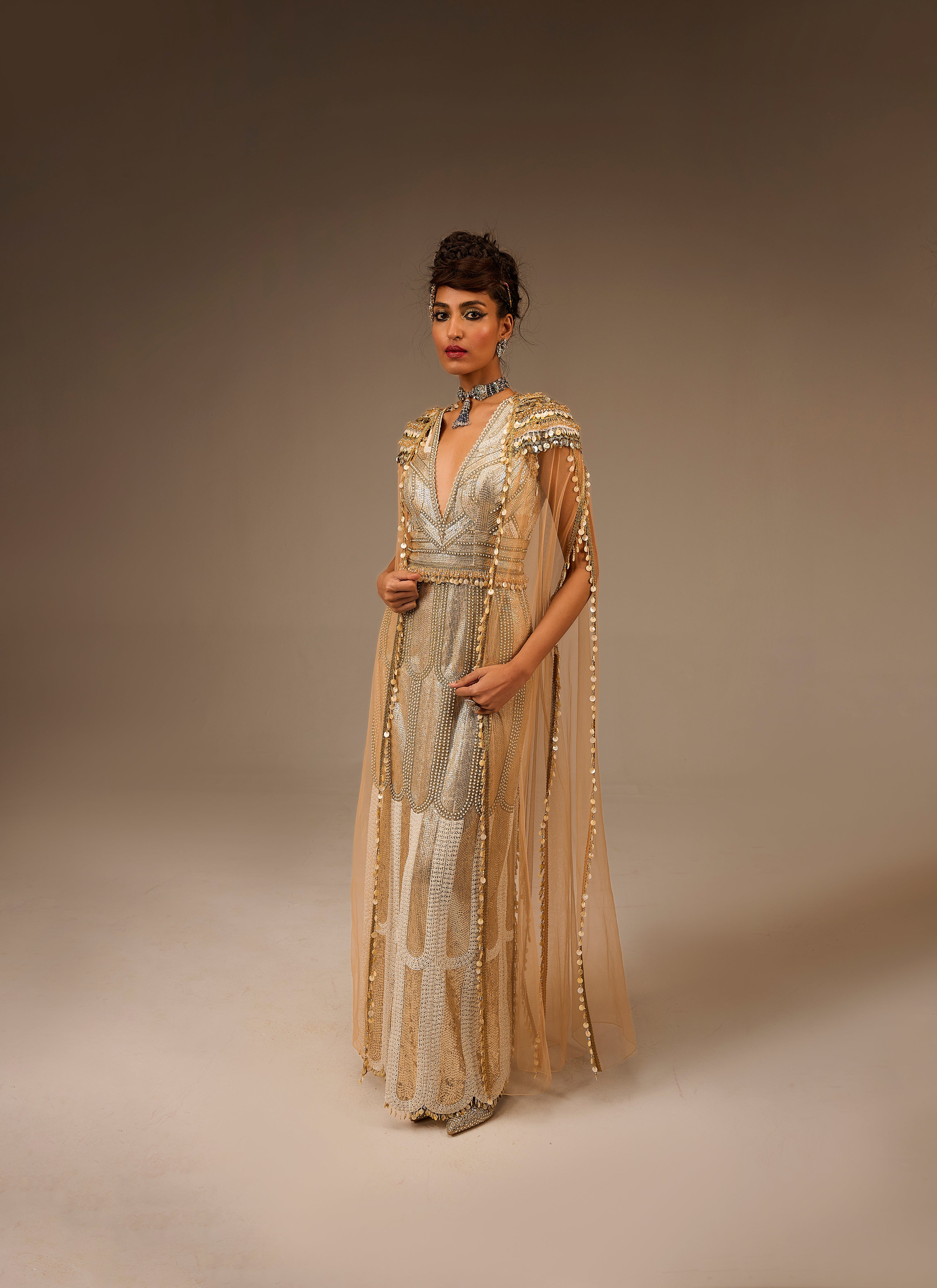 Woman wearing a gold and silver embroidered dress against a brown background