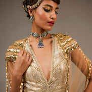 Woman wearing a gold beaded dress with jewelry against a neutral background