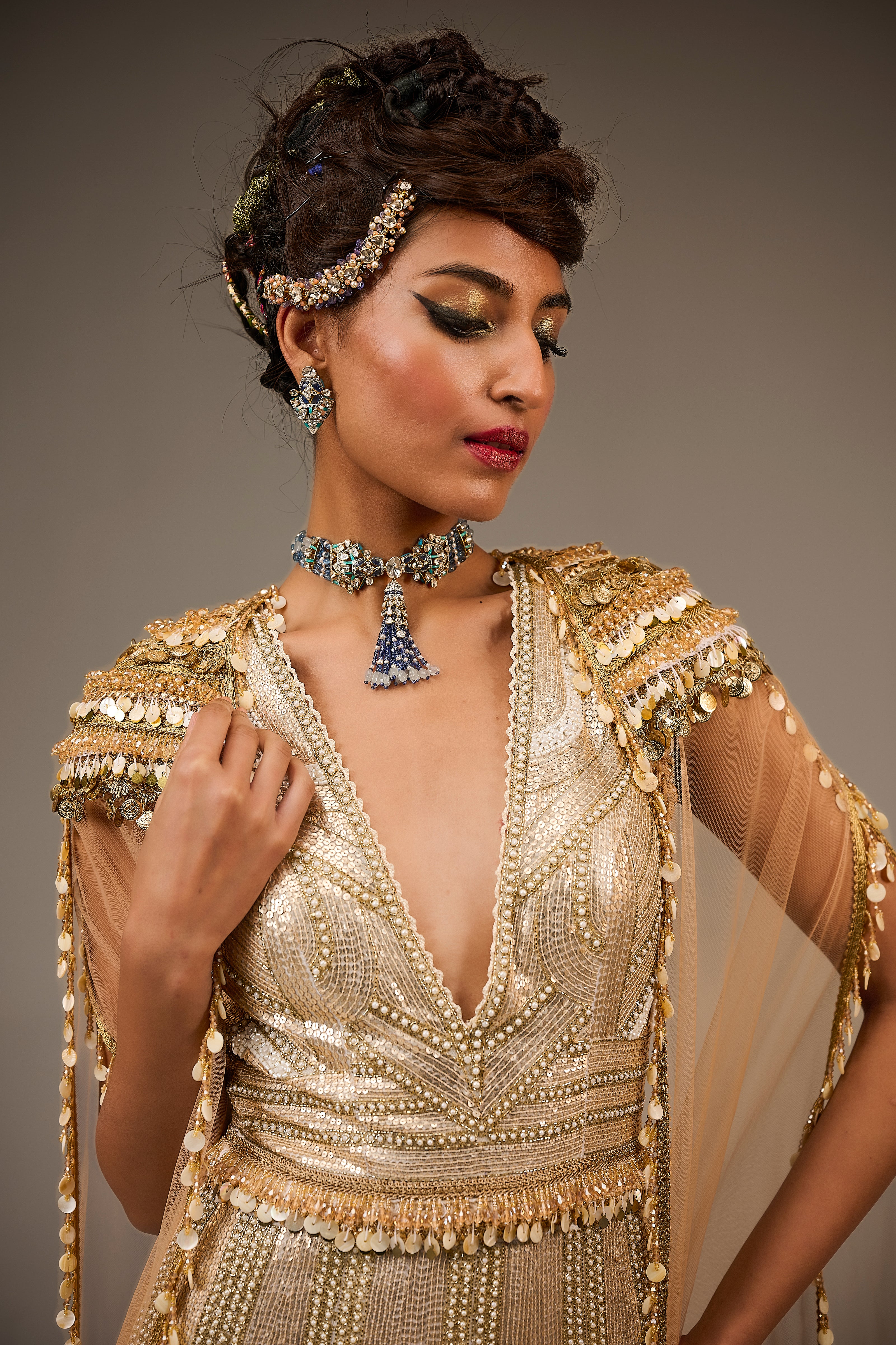 Woman wearing a gold beaded dress with jewelry against a neutral background
