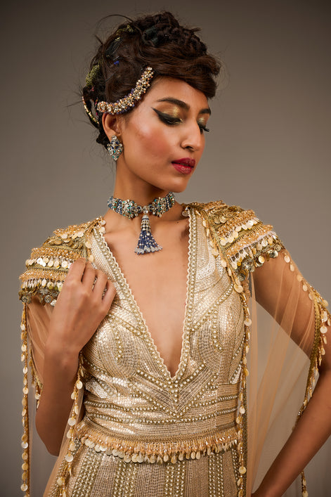 Woman wearing a gold beaded dress with jewelry against a neutral background