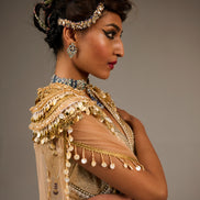 Woman in traditional attire with gold and beige dress and jewelry against a gray background