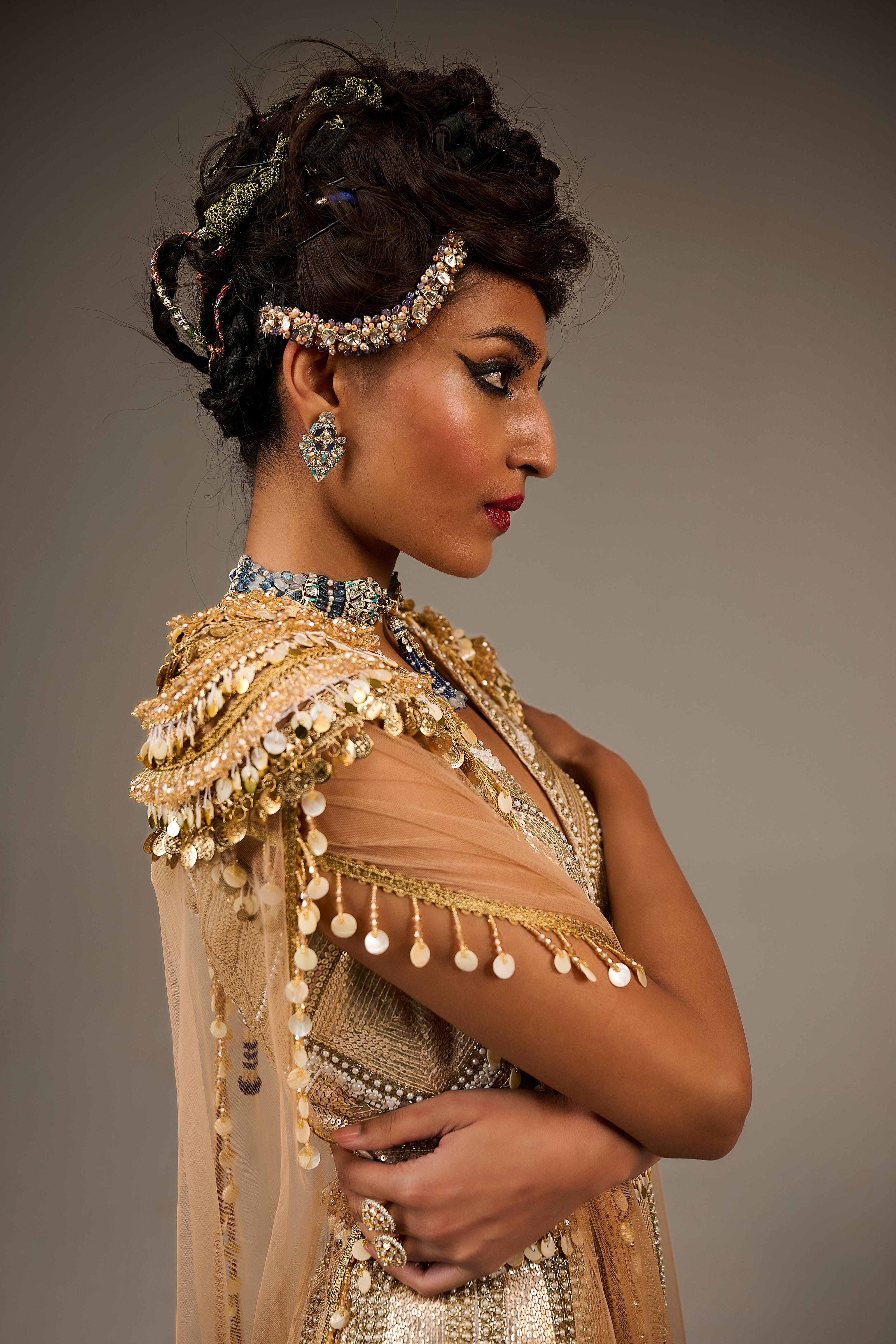 Woman in traditional attire with gold and beige dress and jewelry against a gray background