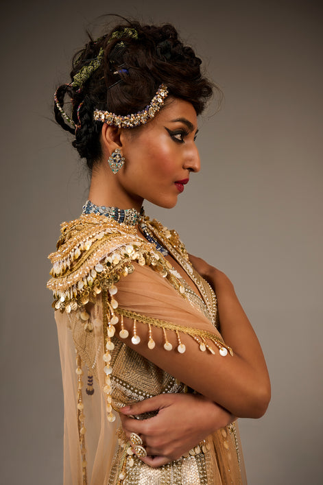 Woman in traditional attire with gold and beige dress and jewelry against a gray background
