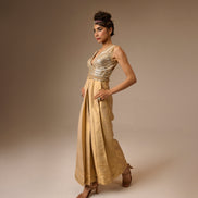 Woman wearing a gold dress with a metallic top and flowing skirt against a beige background