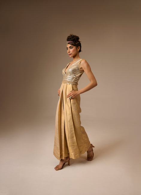 Woman wearing a gold dress with a metallic top and flowing skirt against a beige background
