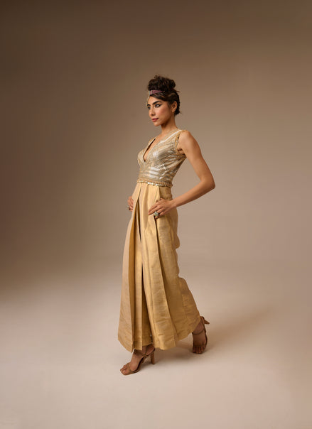 Woman wearing a gold dress with a metallic top and flowing skirt against a beige background