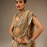 Woman in an ornate, gold embroidered traditional outfit with jewelry against a neutral background