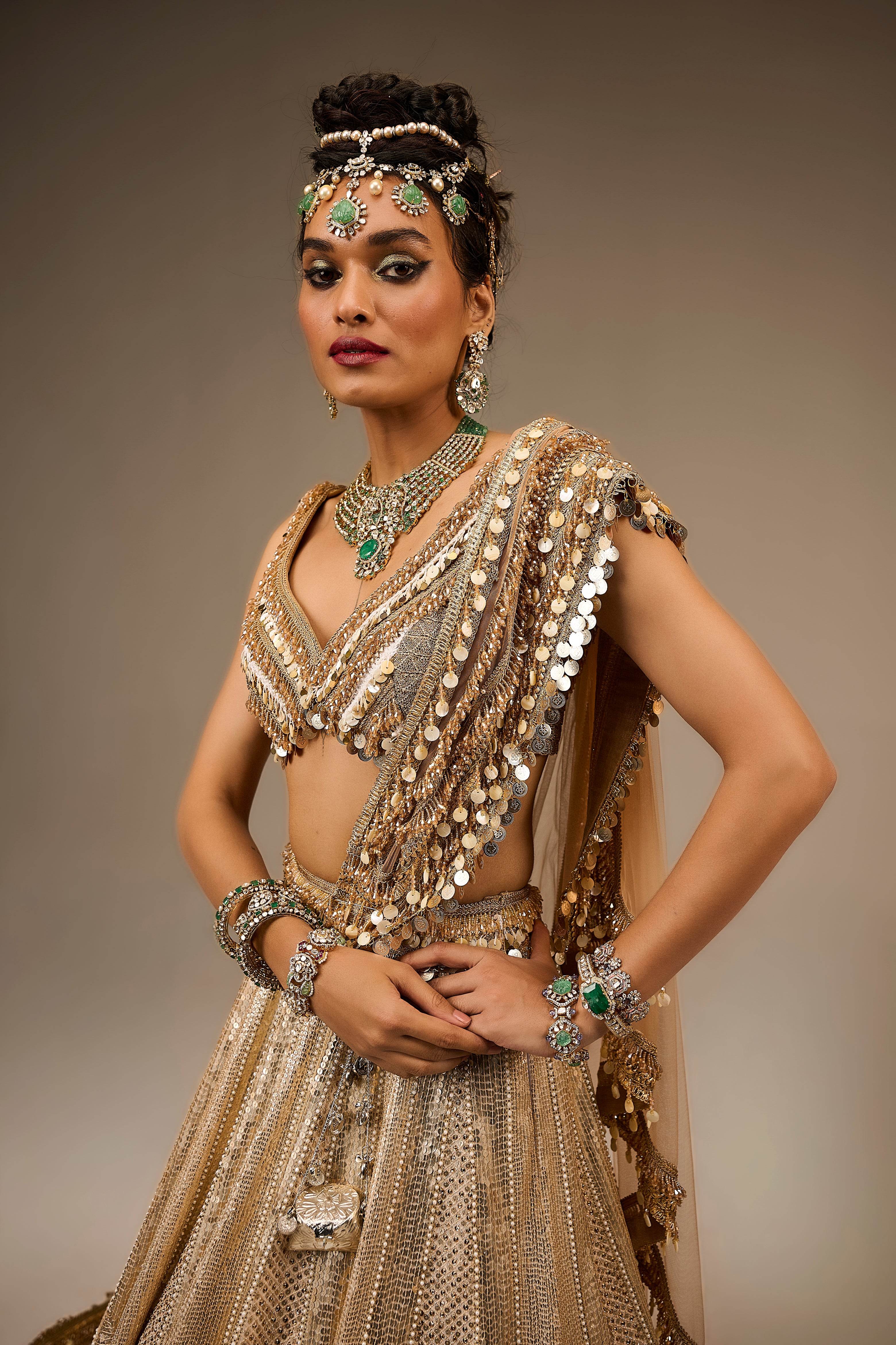 Woman in an ornate, gold embroidered traditional outfit with jewelry against a neutral background