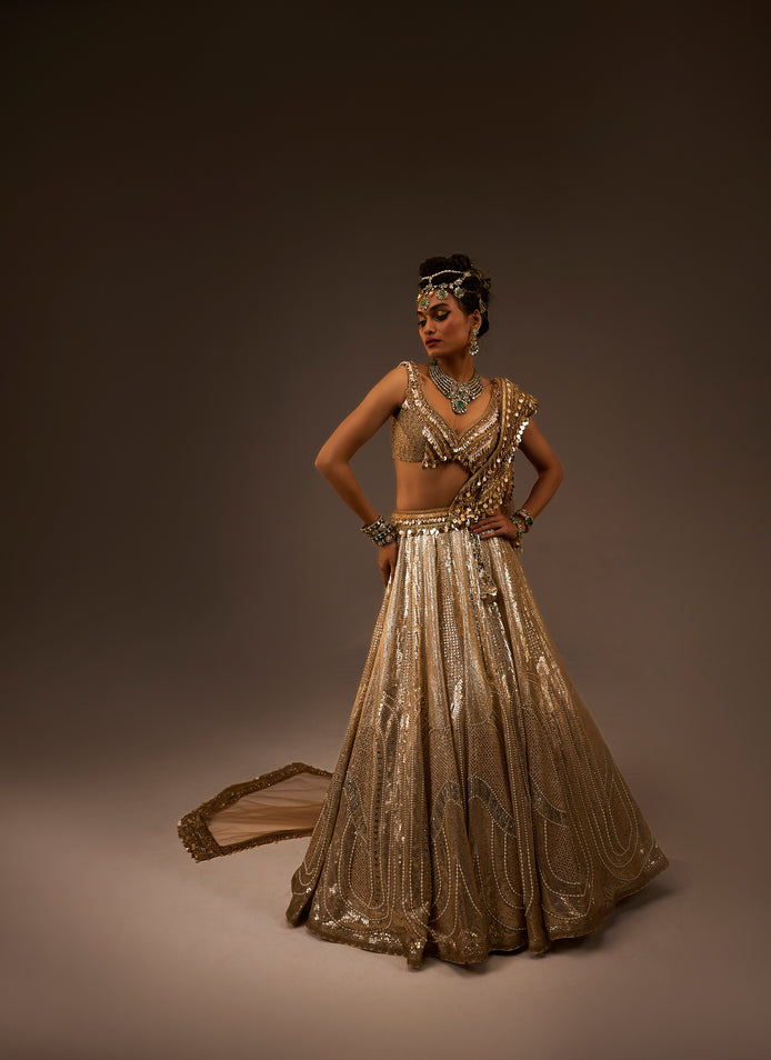Woman in a gold embroidered traditional outfit against a brown background