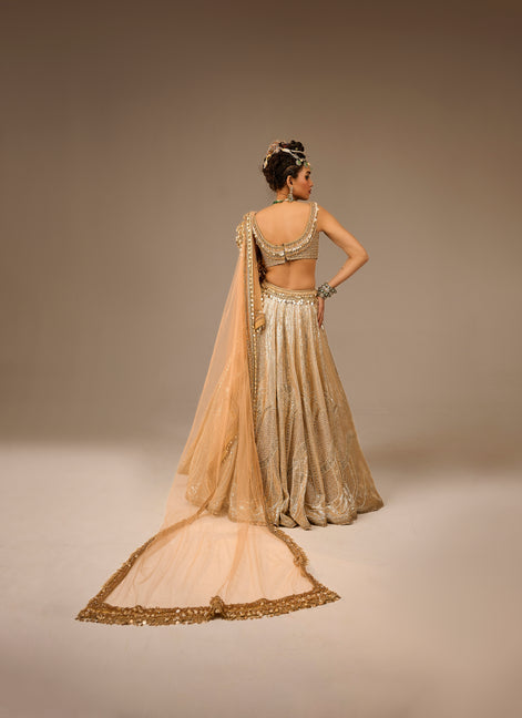 Woman in a traditional beige and gold outfit with a plain background