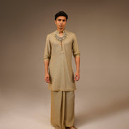 Man wearing a traditional beige kurta with a necklace on a brown background