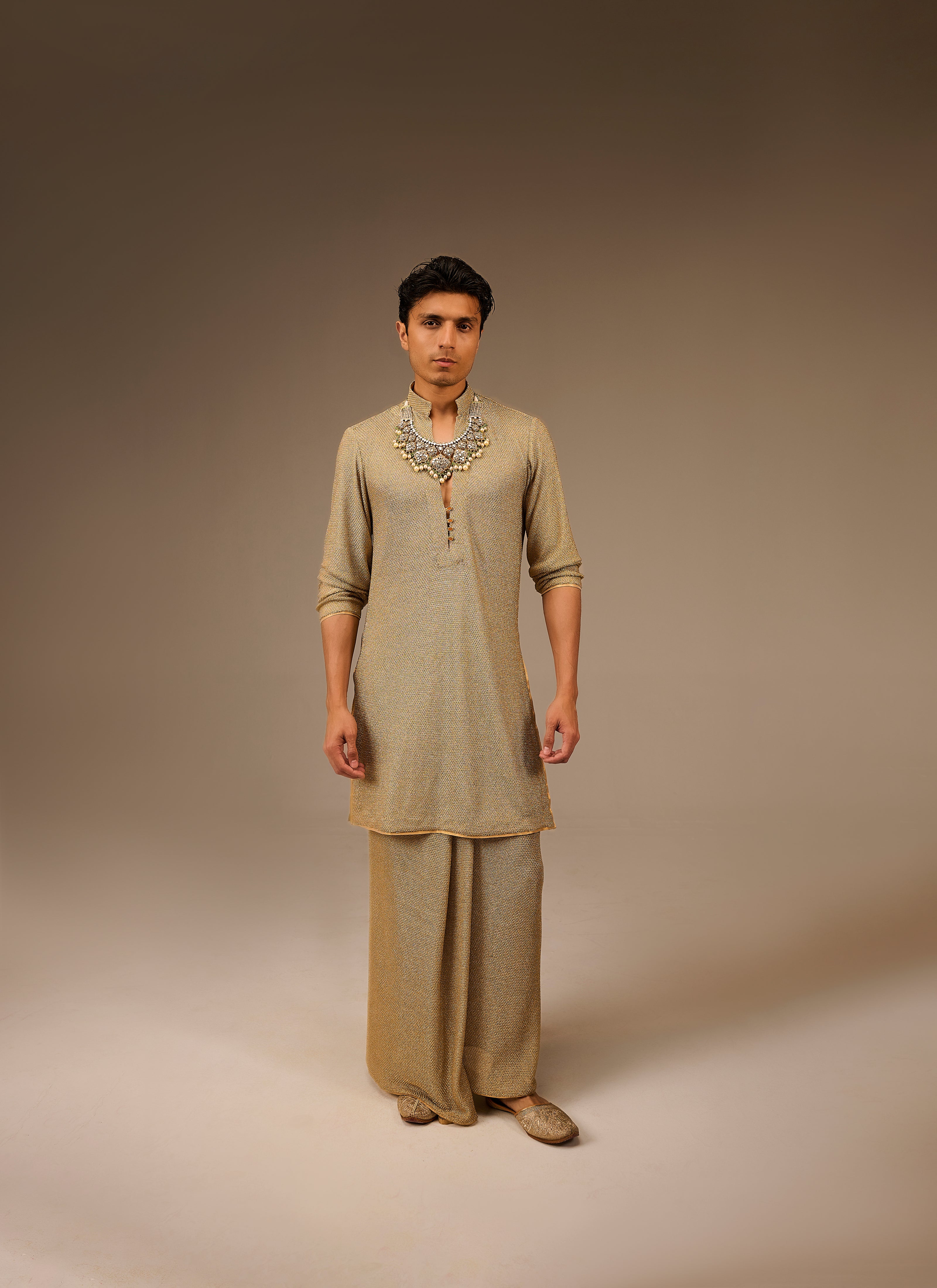 Man wearing a traditional beige kurta with a necklace on a brown background