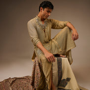Man in traditional attire sitting on a patterned rug against a plain background