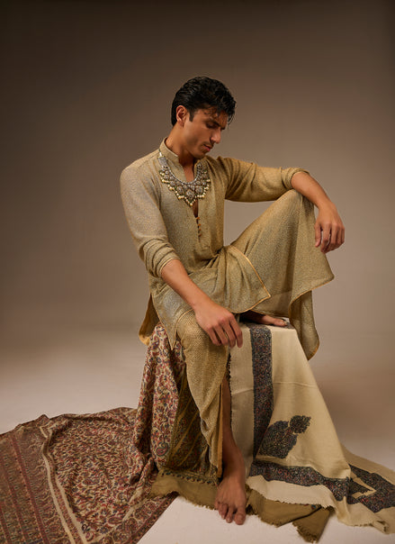 Man in traditional attire sitting on a patterned rug against a plain background