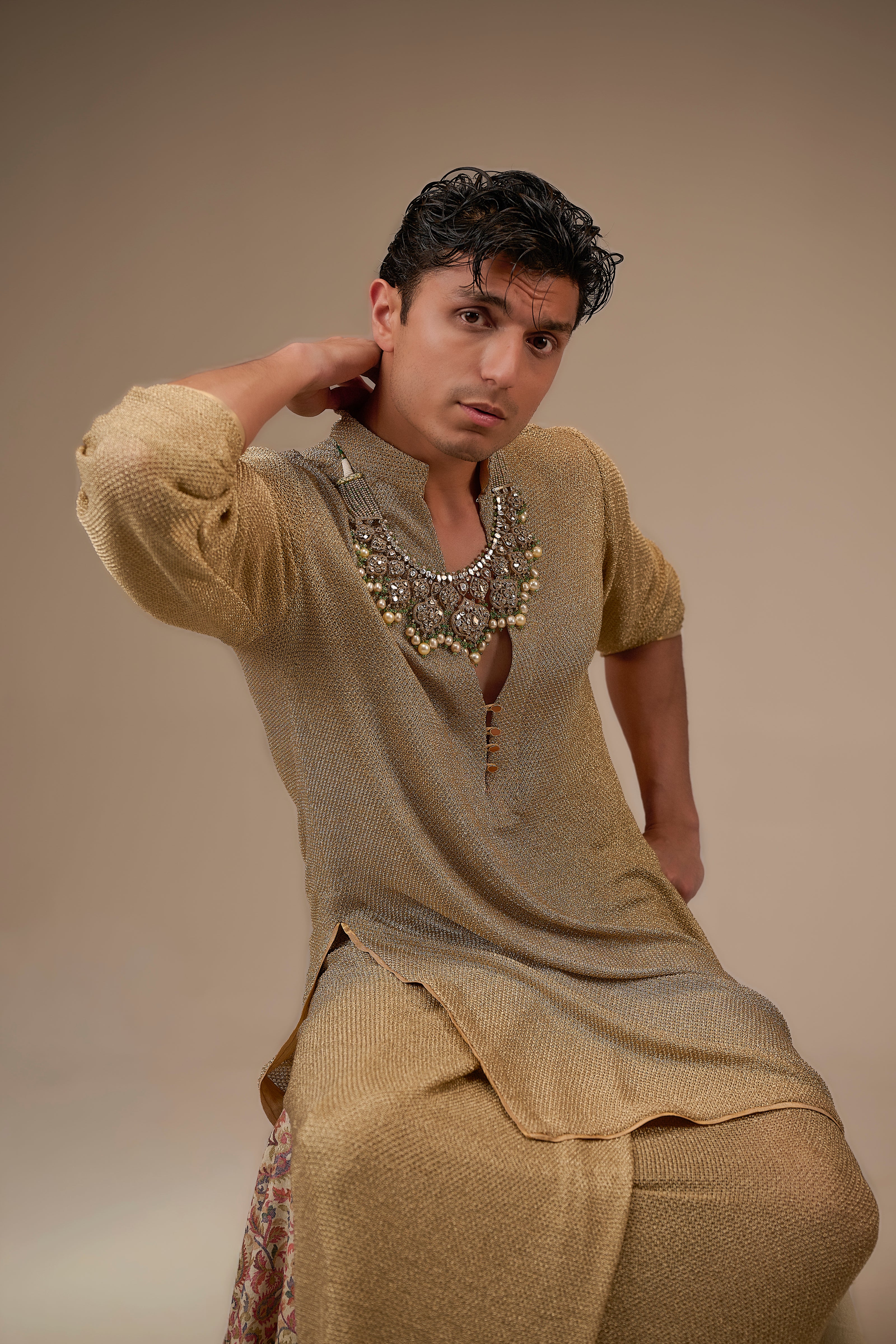Man wearing traditional attire with a necklace against a beige background