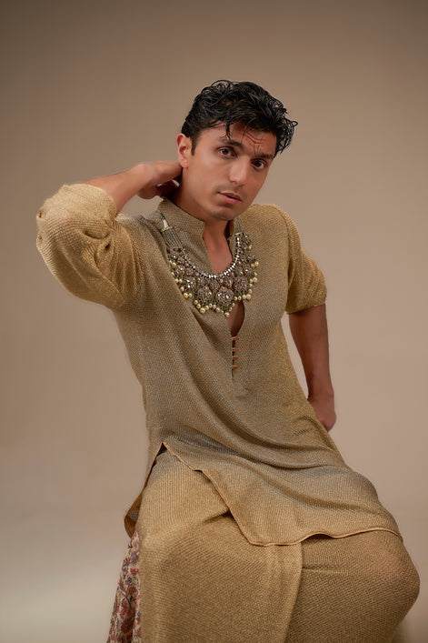 Man wearing traditional attire with a necklace against a beige background