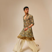 Man wearing a patterned kurta with white pants on a beige background