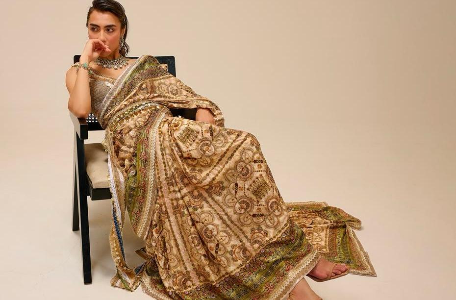 Woman sitting on a chair wearing a traditional patterned saree against a plain background