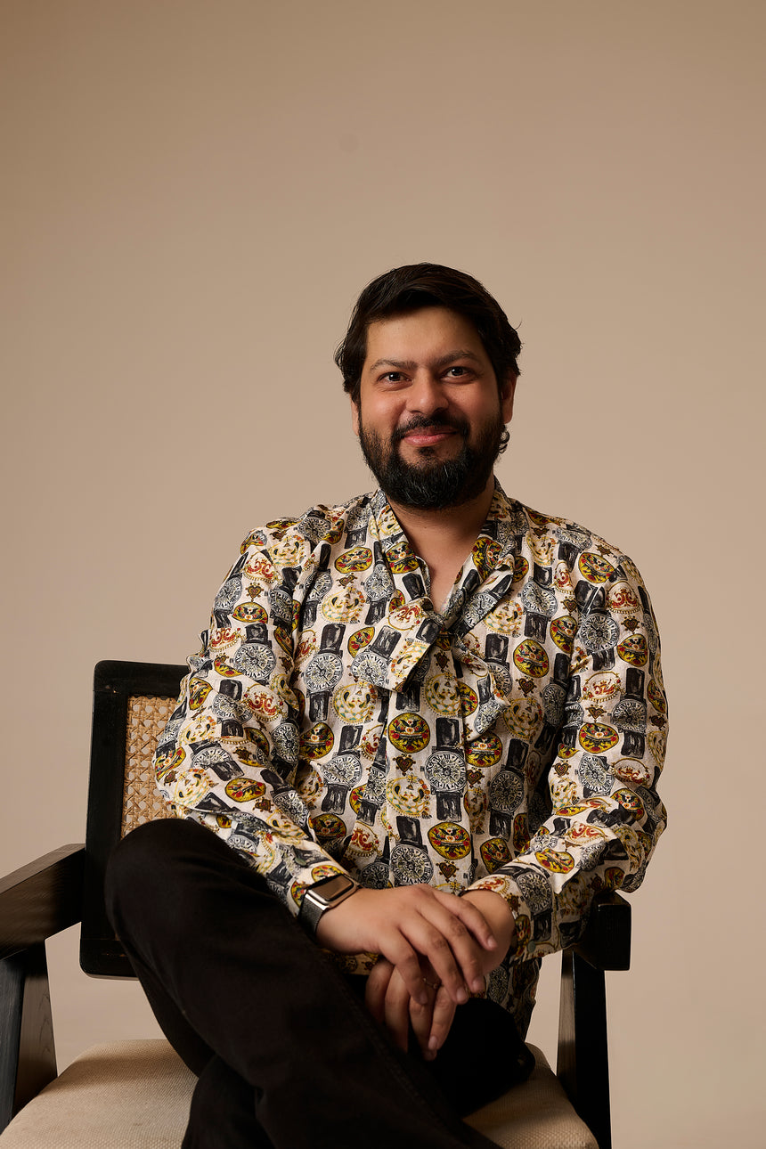Zaib Q sitting on a chair wearing a patterned shirt against a beige background